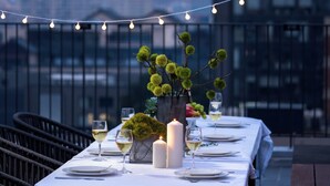 Un espace de restauration aménagé sur le toit, avec une table pour deux, des guirlandes lumineuses, des bougies et une plante décorative en guise de centre de table.