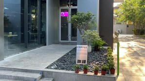 Une entrée moderne avec une porte en verre, une enseigne indiquant « CAFÉ CAFÉ CAFÉ » et un petit espace jardin agrémenté de plantes en pot.