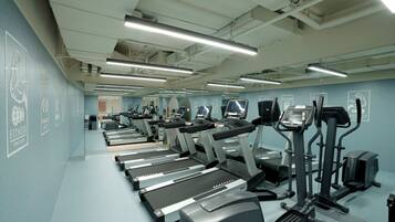 A gym with multiple treadmills and elliptical machines, a mirrored wall, and a blue wall with fitness-related graphics.