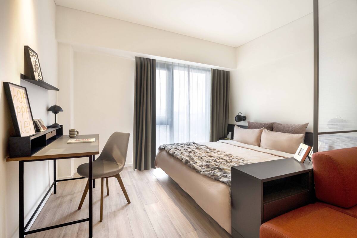 A modern hotel room with a bed, a desk, a chair, and a sofa.