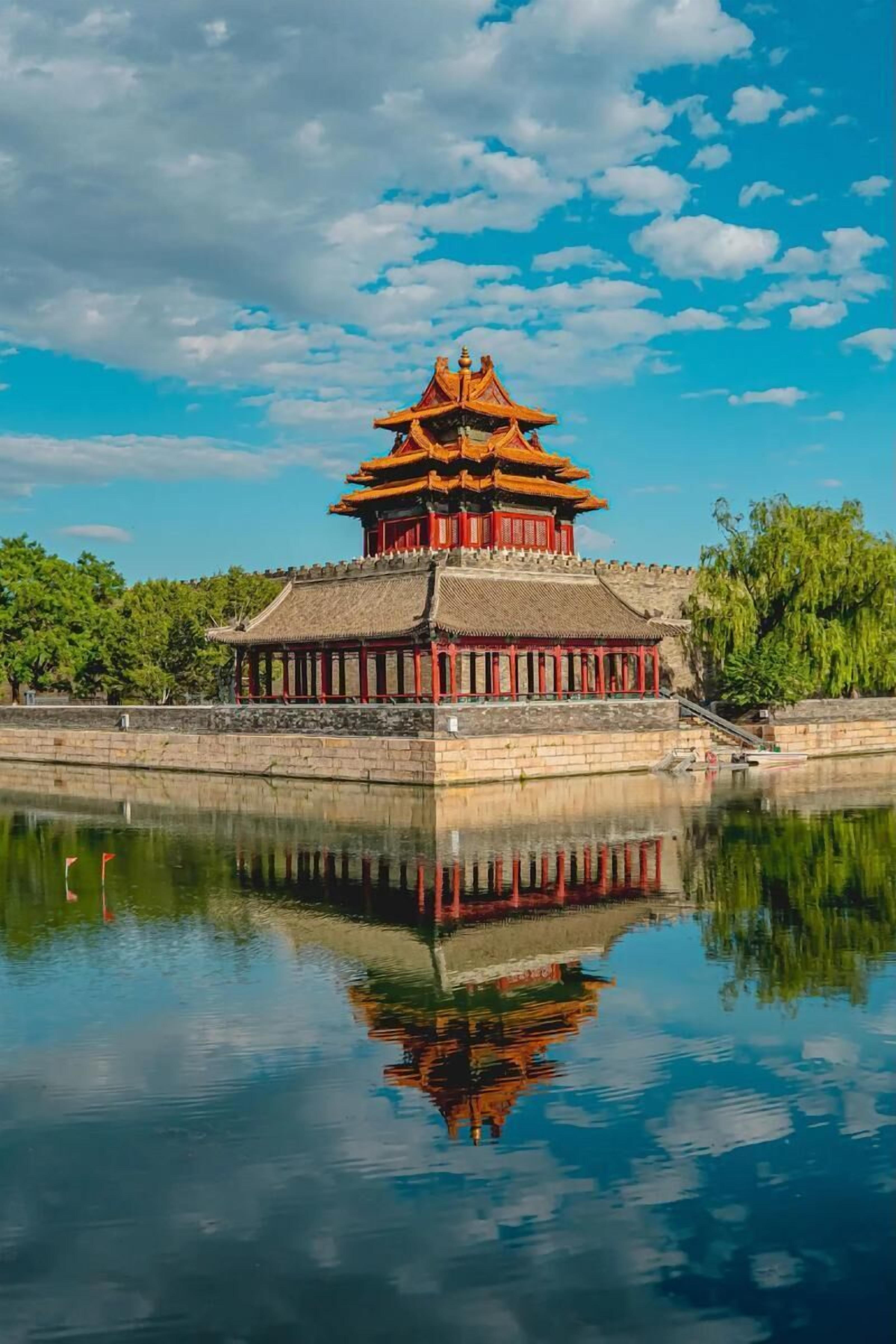 A traditional Chinese building with a multi-tiered roof, reflecting in a calm body of water.