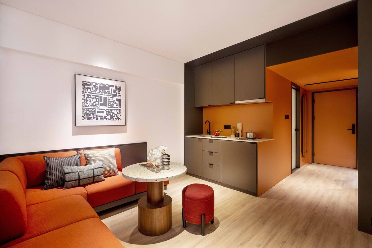 A modern living room with a sofa, a round table, and a red ottoman.