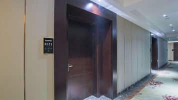 A hotel corridor with a carpeted floor, a wooden elevator, and a door with a sign.