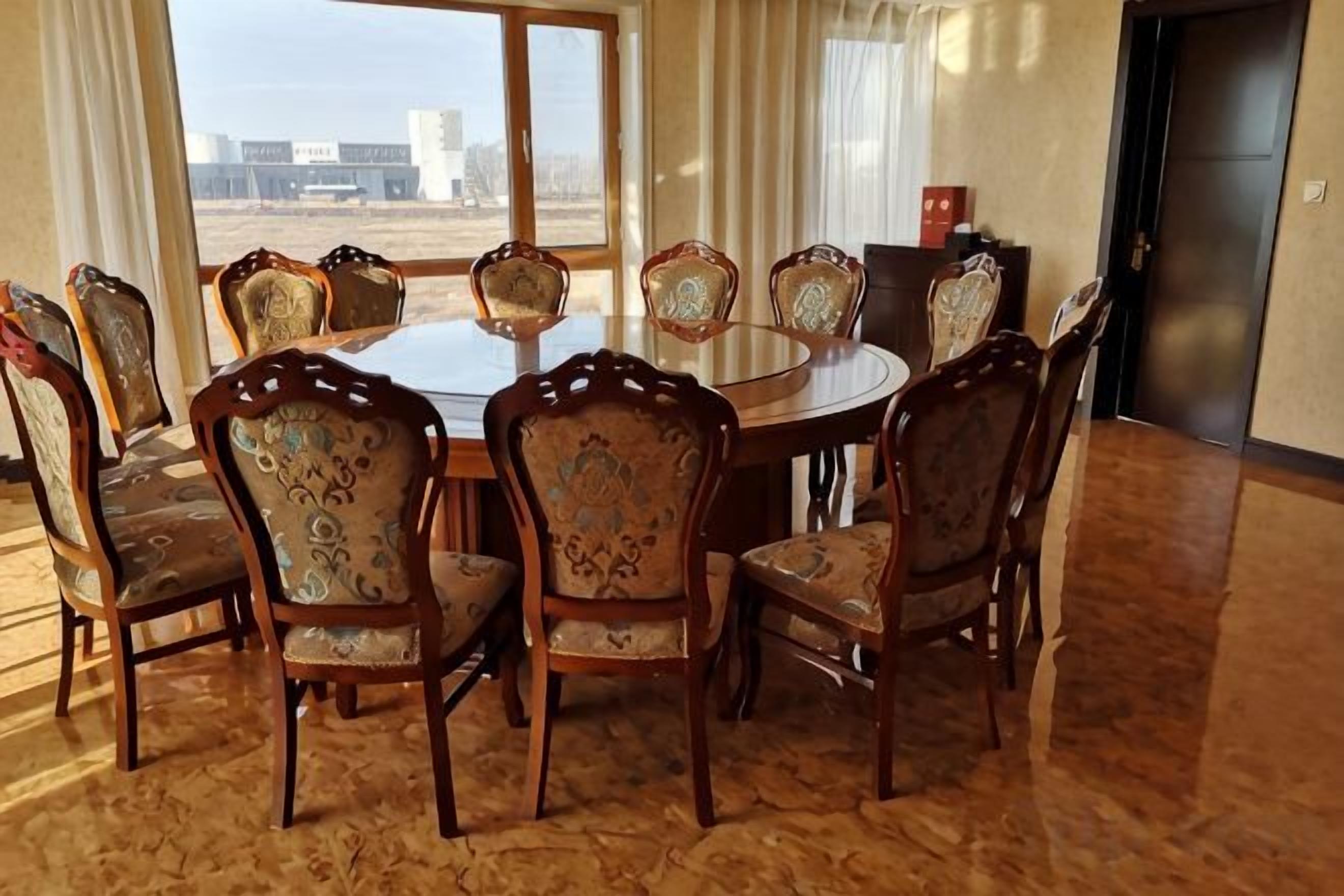 A conference room with a round table and eight chairs, large windows with curtains, and a door.