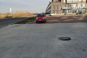 Uma área de estacionamento com um carro vermelho estacionado perto de um edifício com sinalização.