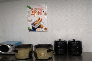 A kitchen with two large cooking pots, a microwave, and a poster on the wall. - Fangzheng Golden Lake Hotel (High-speed Railway Station) (Fangzheng)