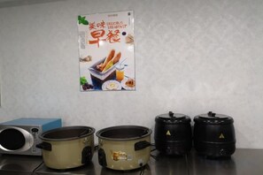 Een keuken met drie kookpotten op het aanrecht, een magnetron en een poster aan de muur.