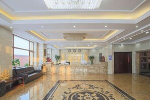 Een hotellobby met een receptiebalie, een zithoek en een kroonluchter.