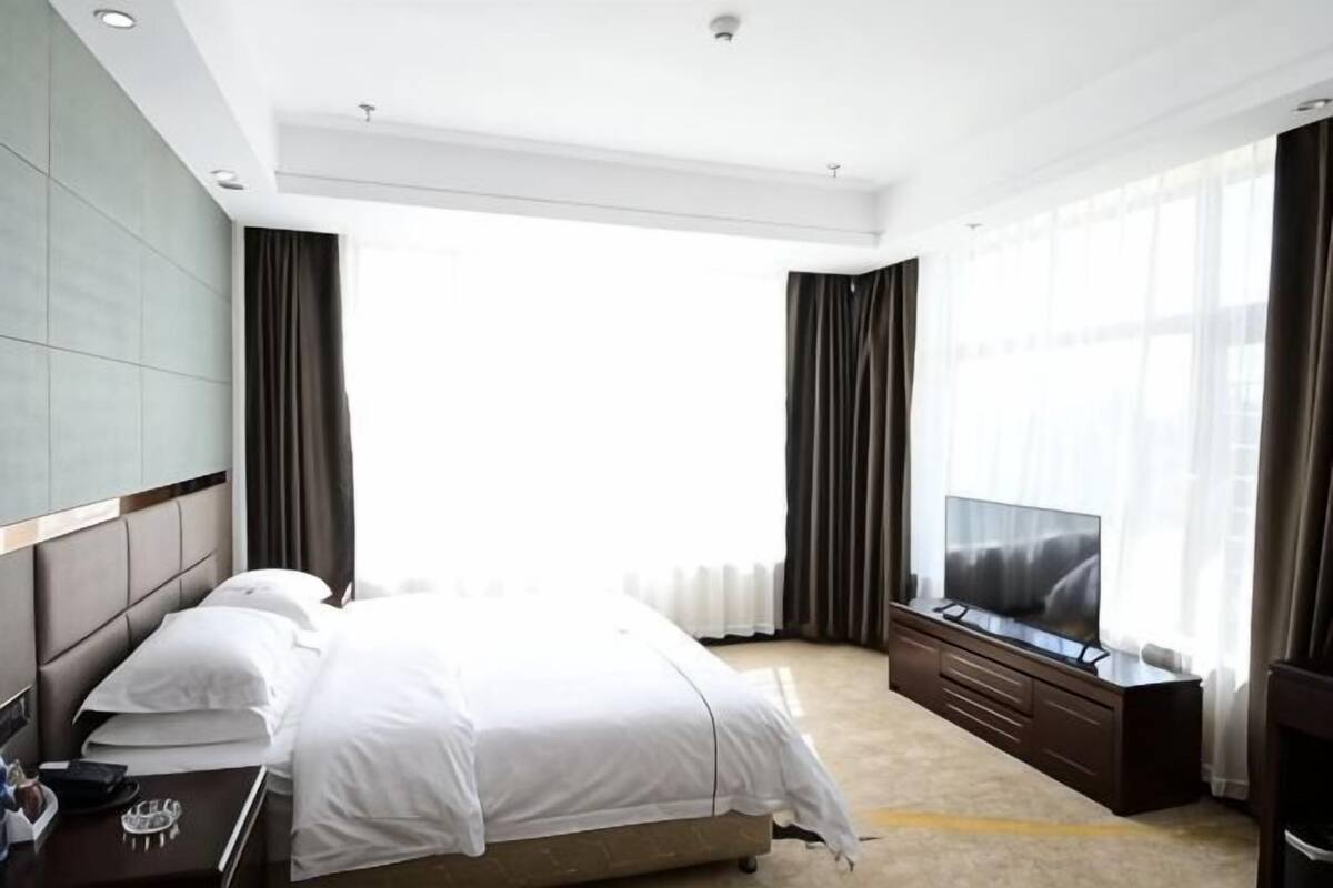 Hotelkamer met een groot bed, een televisie, een zithoek met een bank en een groot raam met gordijnen.