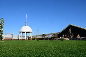 Een witte koepelstructuur met een vlaggenmast, een overdekte paviljoen met beelden en een grasveld.