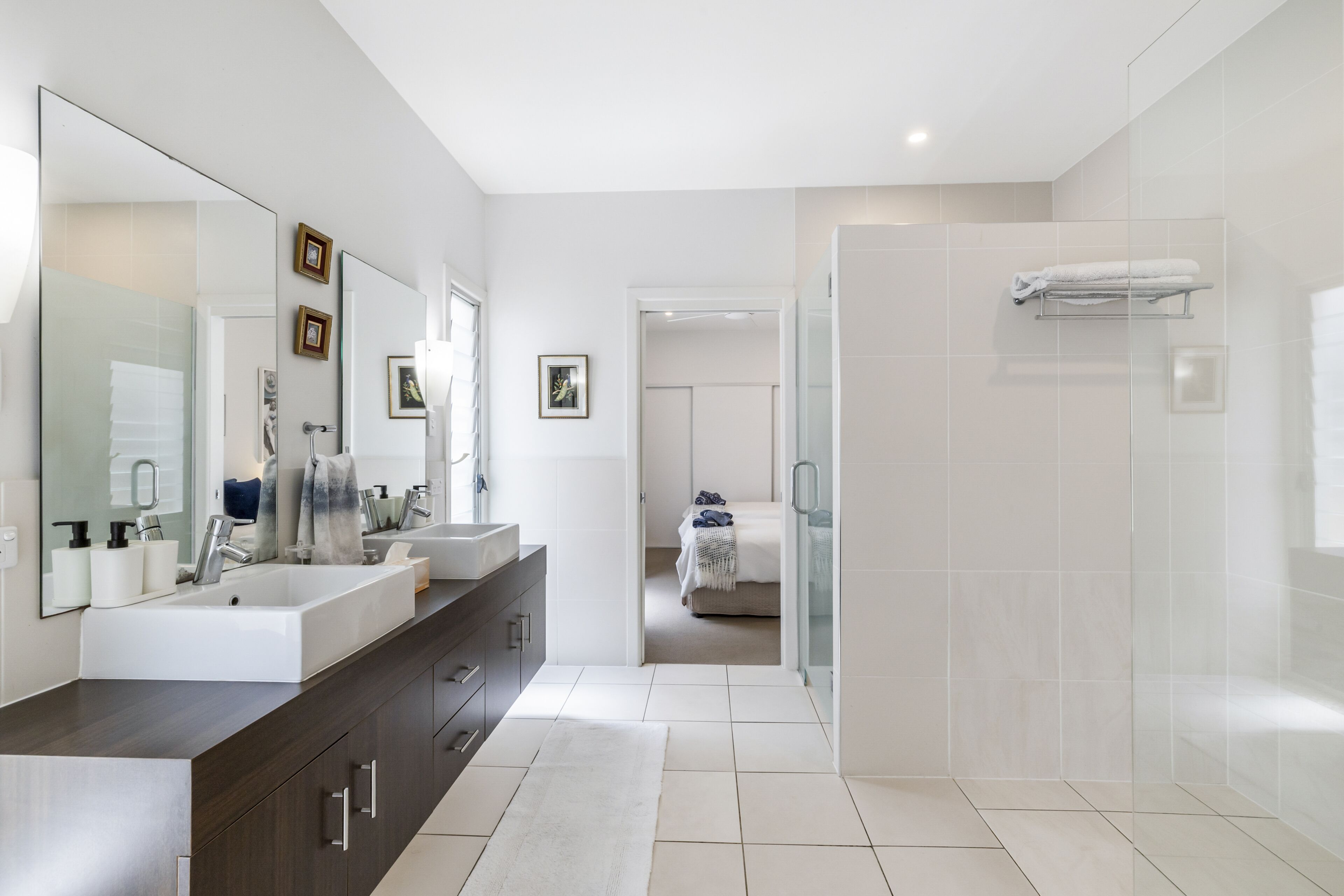 Een moderne badkamer met een grote spiegel, twee wasbakken, een donkere badkamermeubel en een inloopdouche.