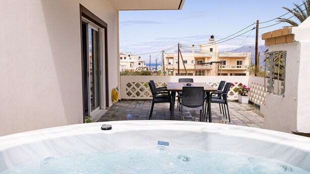 A hot tub with a table and chairs, a tiled patio, and a view of buildings in the background. - Villa panagiotis (Κίσσαμος)