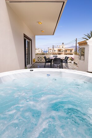 Een hottub met een tafel en stoelen, een betegeld terras en gebouwen op de achtergrond.