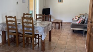 Un coin repas avec une table dressée pour quatre personnes, un téléviseur posé sur un meuble et un canapé agrémenté de coussins.