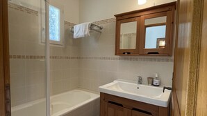 Une salle de bain avec une baignoire, un lavabo, des meubles en bois, un miroir et une fenêtre agrémentée d’un panneau de verre décoratif.