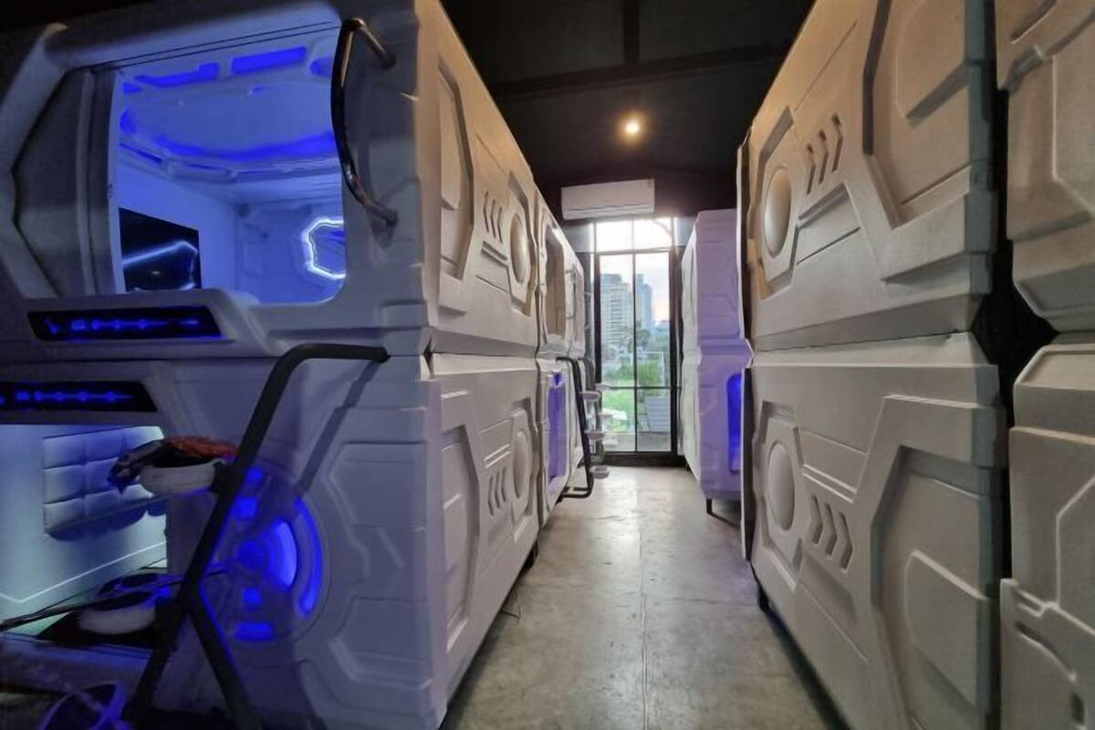 A corridor with stacked bunk beds and a blue-lit room on the left.