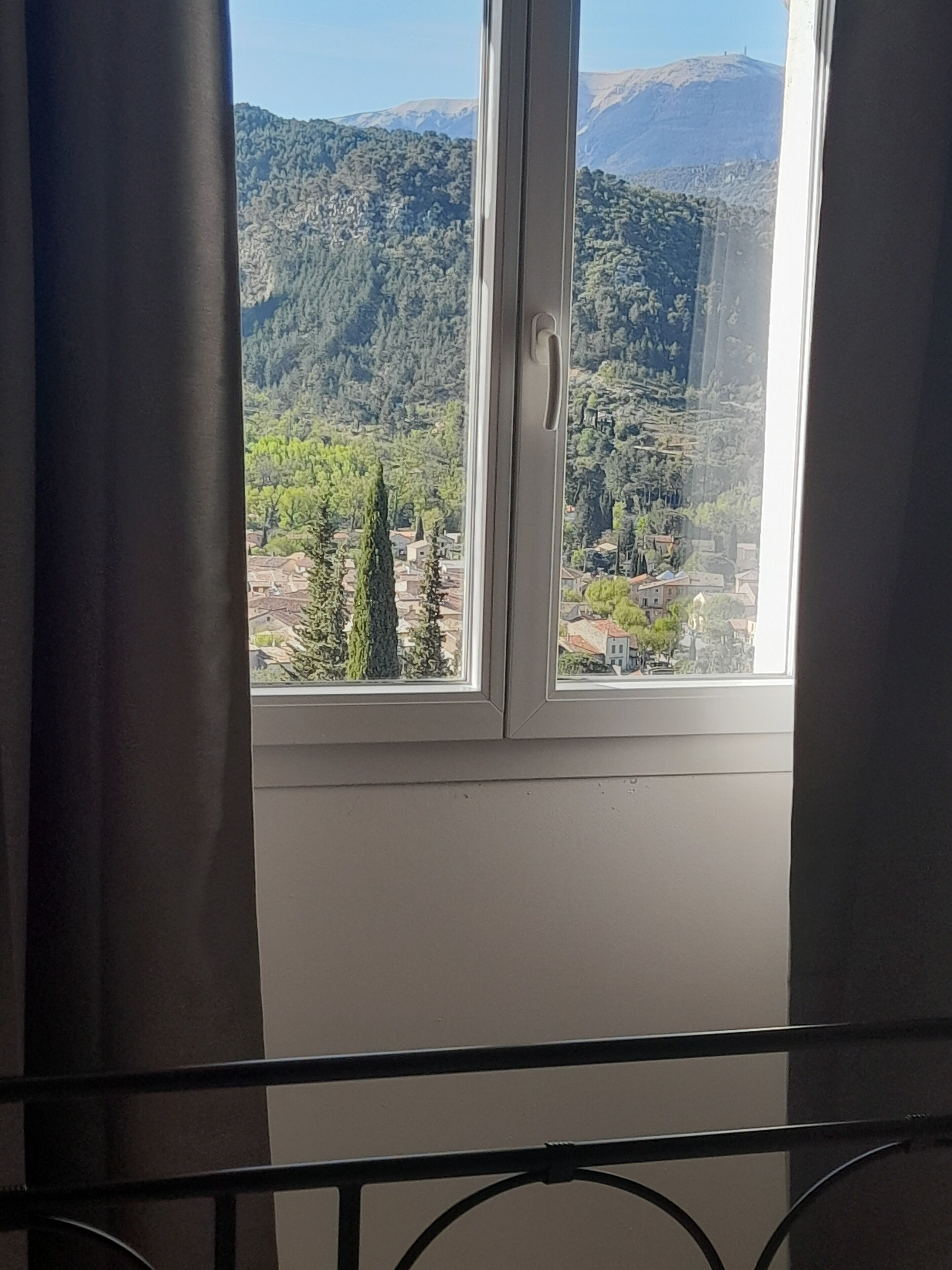 Une fenêtre donnant sur un paysage montagneux et un village situé en contrebas.
