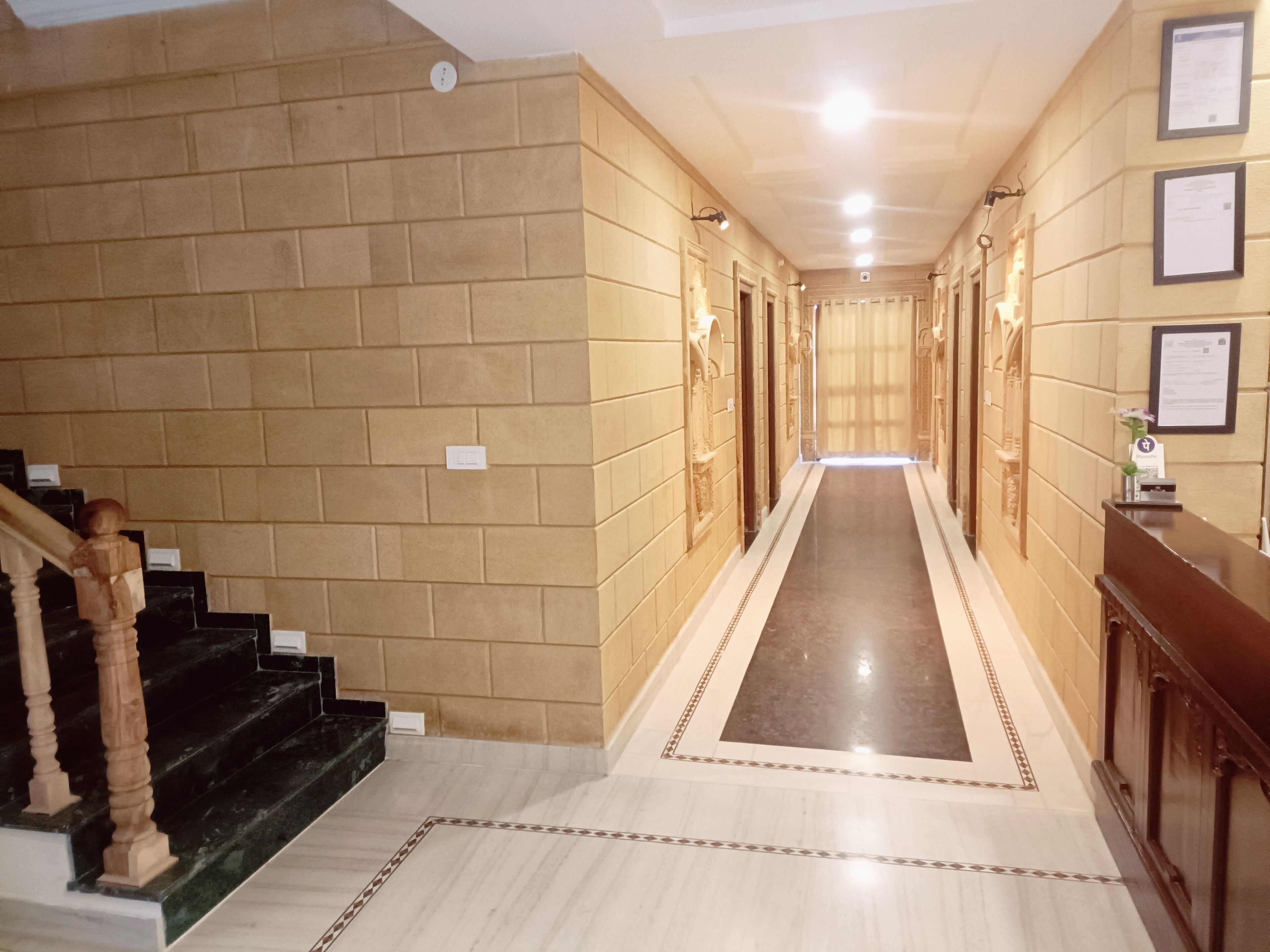 Un corridoio d'albergo con una scalinata in marmo, una reception e un lungo corridoio con porte su entrambi i lati.