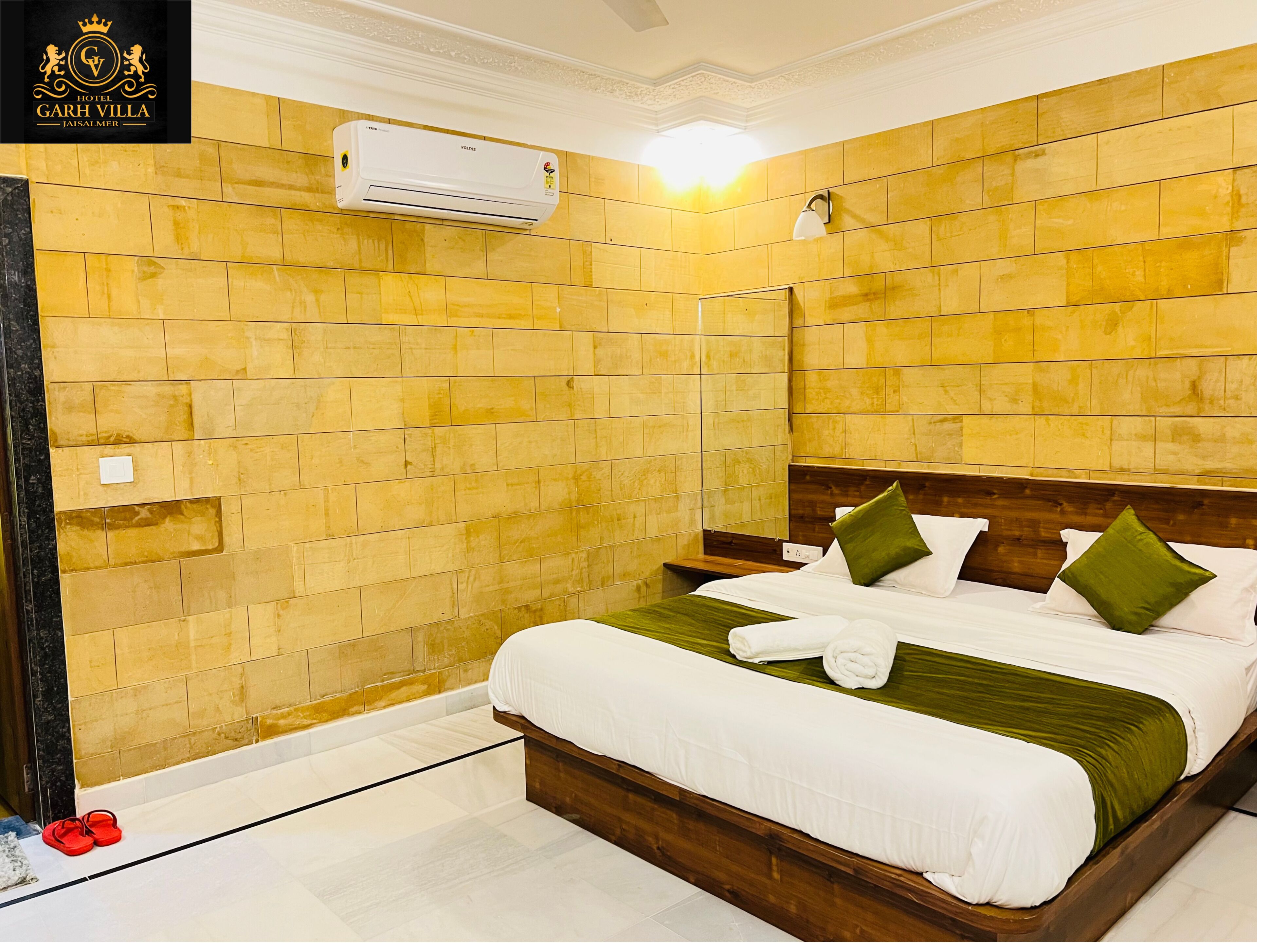 Ein Hotelzimmer mit einem hölzernen Kopfteil, einem Bett mit weißer Bettwäsche und grünen Kissen, einer Klimaanlage und einer gefliesten Wand.