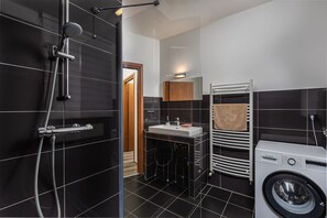 A modern bathroom with a black and white tiled floor, a shower, a sink, a towel rack, and a washing machine. - Venus Apartments - King Street V (Budapest)