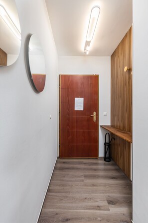 Stylish hallway with a door, mirror, and shelf, set against a backdrop of white walls and a light-colored floor.