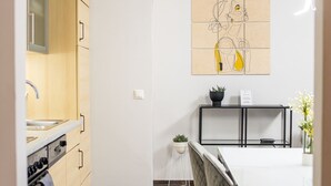 Moderni keittiö, jossa on puiset kaapit, valkoinen työtaso sekä ruokailutila, jossa on lasipöytä ja -tuolit.