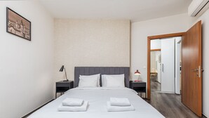 Moderni hotellihuone, jossa on suuri sänky, kaksi yöpöytää, yölamppu, seinällä oleva kehystetty taulu ja puinen ovi.