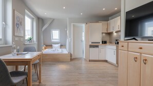 Un espacio habitable moderno y compacto con kitchenette, comedor y dormitorio.