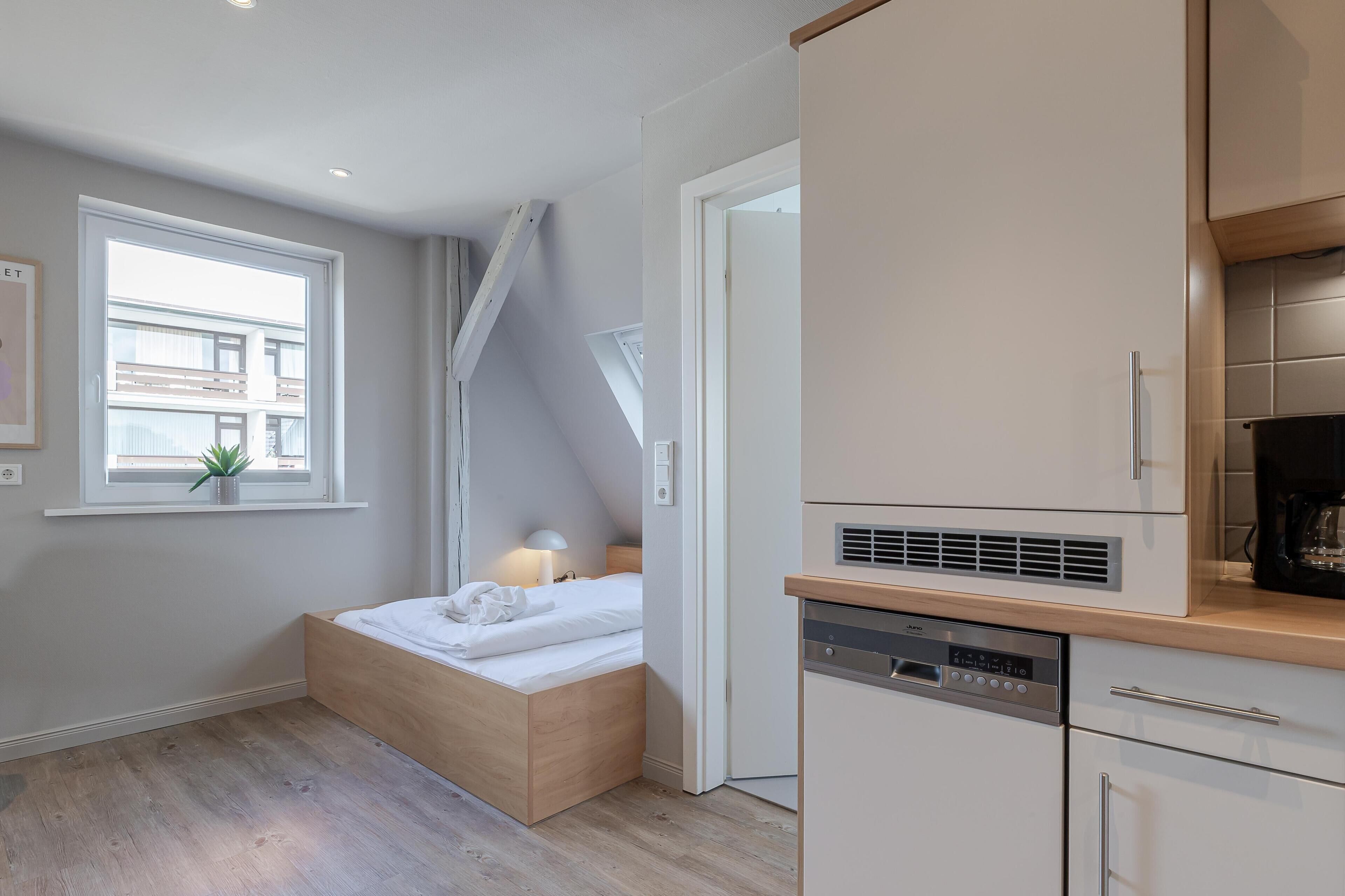 Un dormitorio compacto con cama empotrada, una mesita de noche pequeña y un ventanal con vistas a edificios.