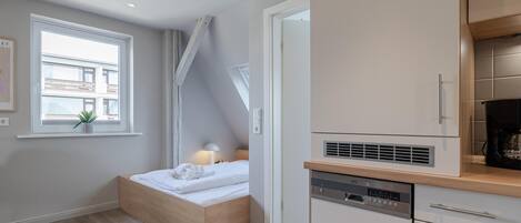 Un dormitorio compacto con cama empotrada, una mesita de noche pequeña y un ventanal con vistas a edificios.