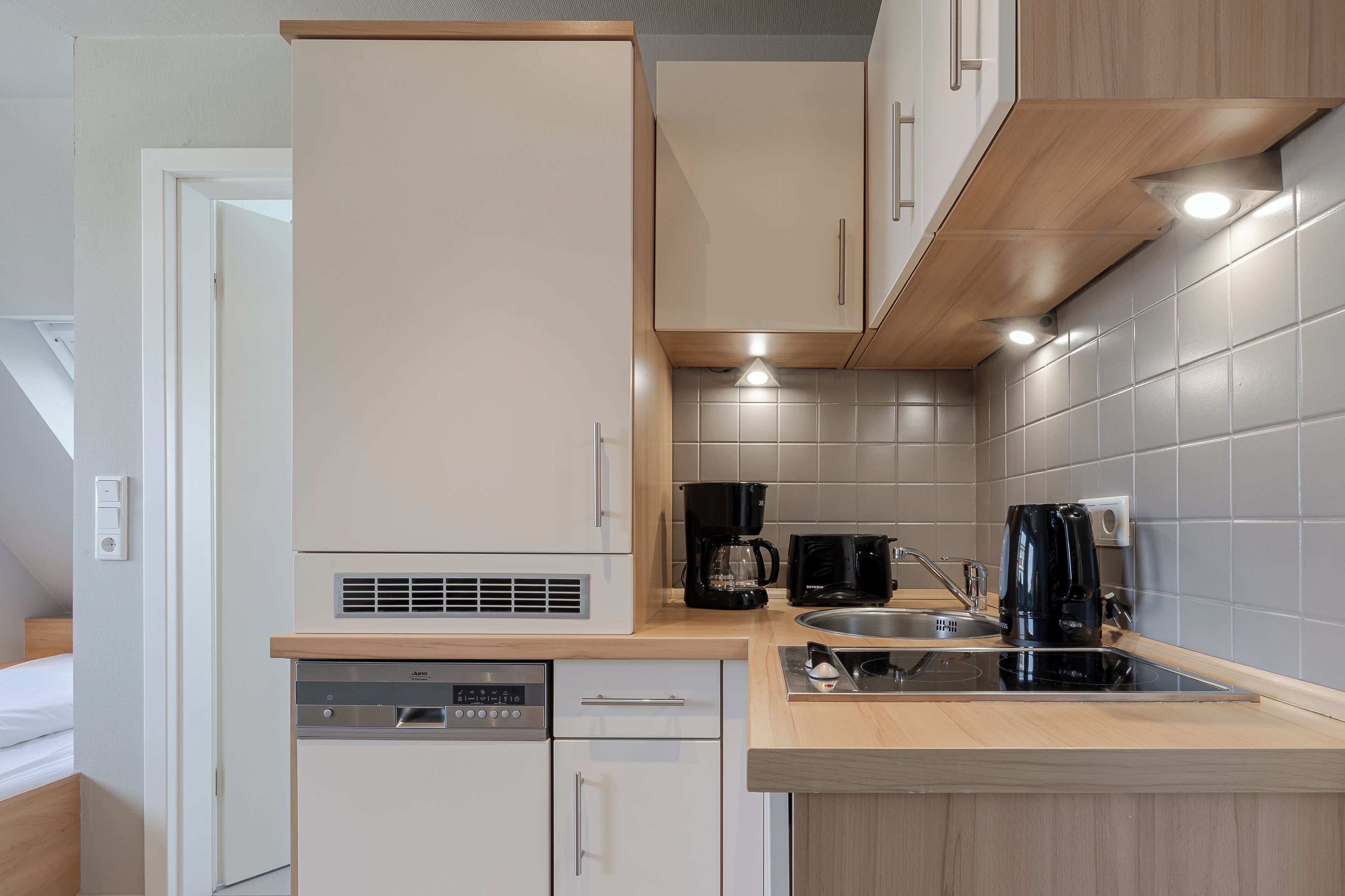 A compact kitchen with a dishwasher, coffee maker, and a sink.