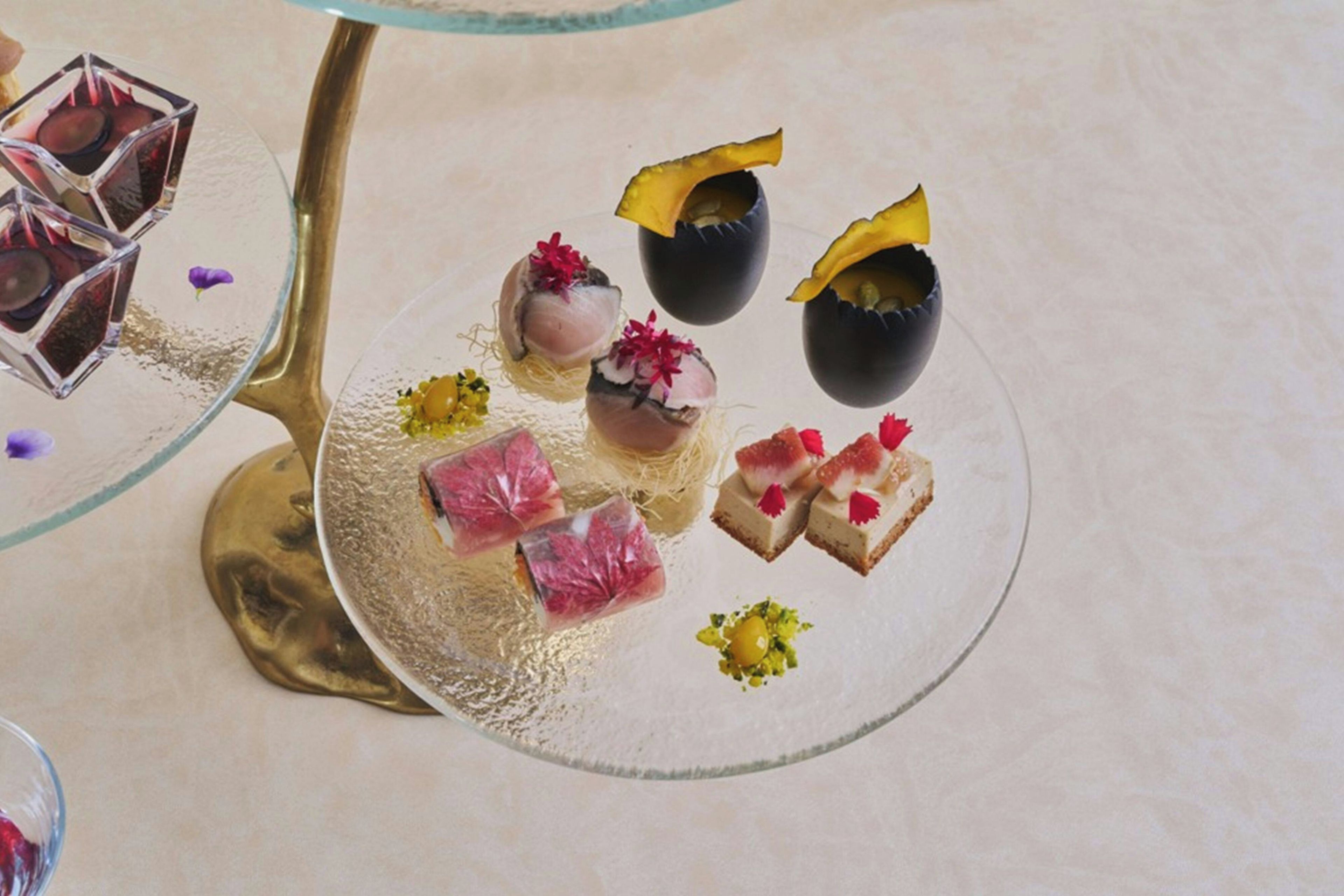 A dessert plate with various items including a clear glass cube, a golden stand, and a white plate with food items.