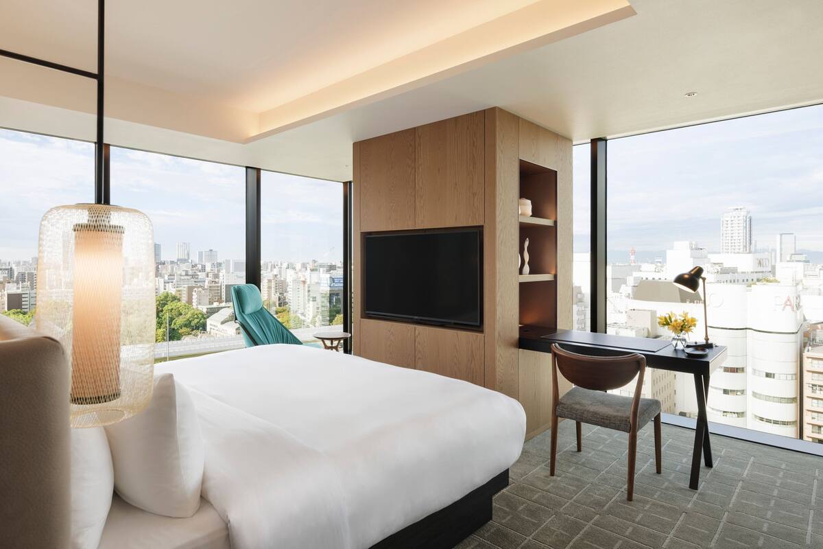 A modern hotel room with a large bed, a desk, a TV, and a city view.