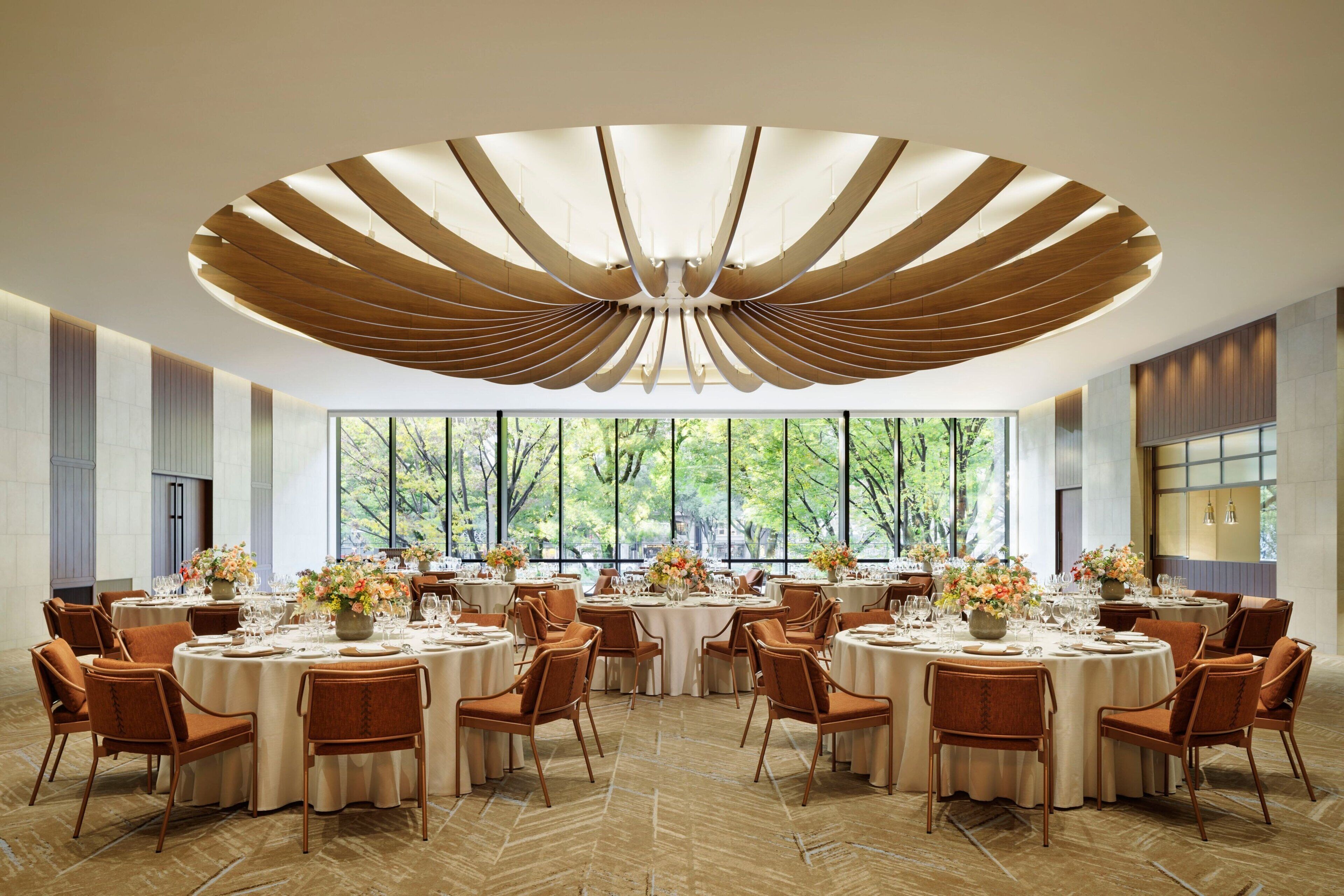 A spacious dining area with round tables, chairs, and large windows offering a view of trees.