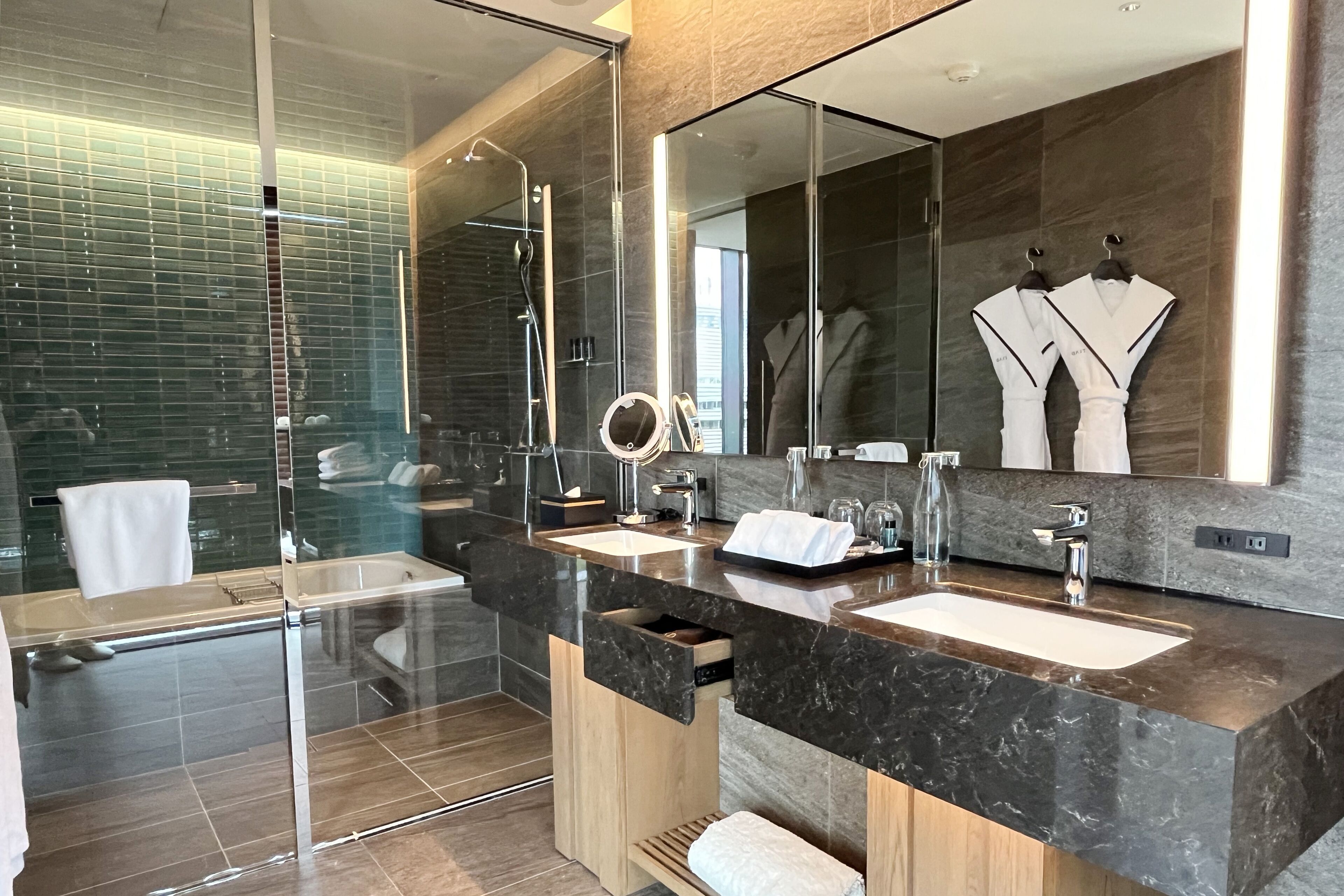 Une salle de bain moderne avec une douche à l’italienne en verre, deux lavabos, un meuble-lavabo et un grand miroir.