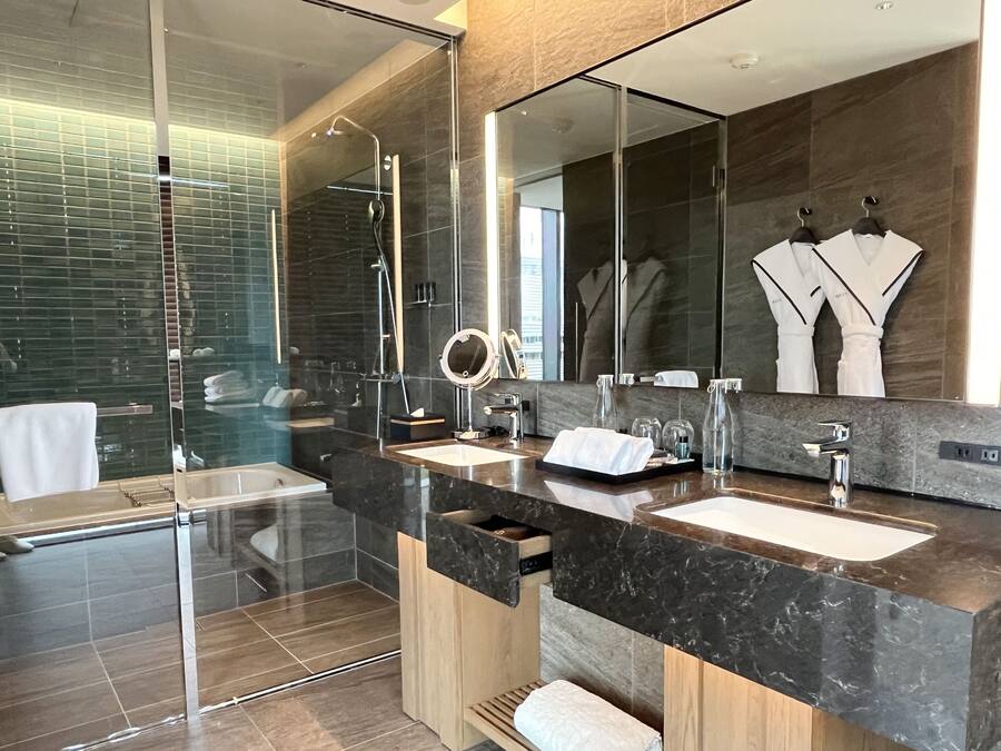 Une salle de bain moderne avec une douche à l’italienne en verre, deux lavabos, un meuble-lavabo et un grand miroir.