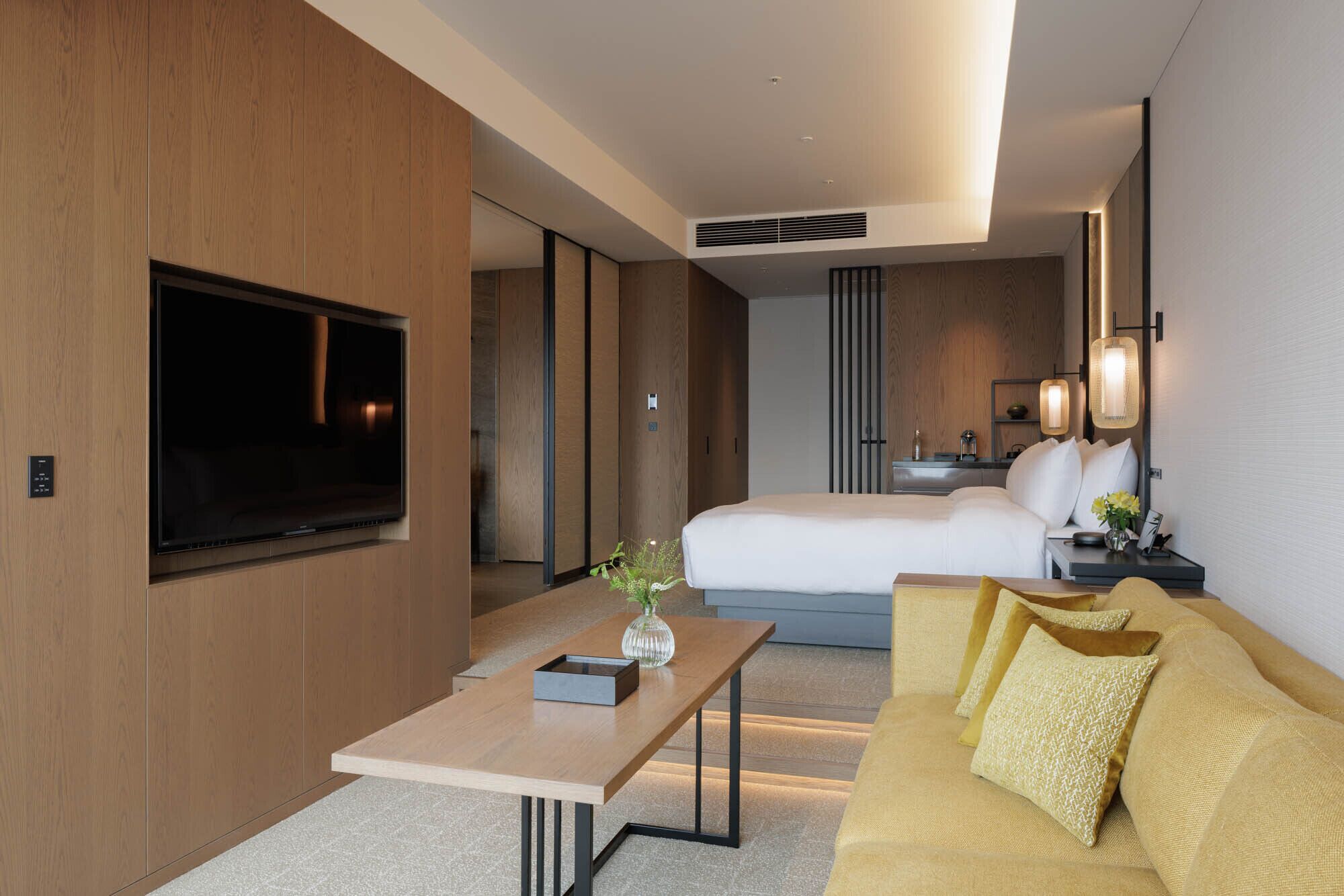 A modern hotel room with a large bed, a sofa, a TV, and a desk with a vase.