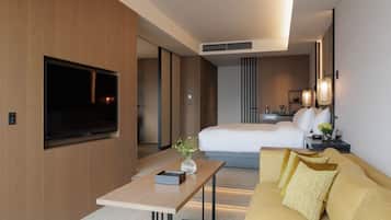 A modern hotel room with a large bed, a sofa, a TV, and a desk with a vase.