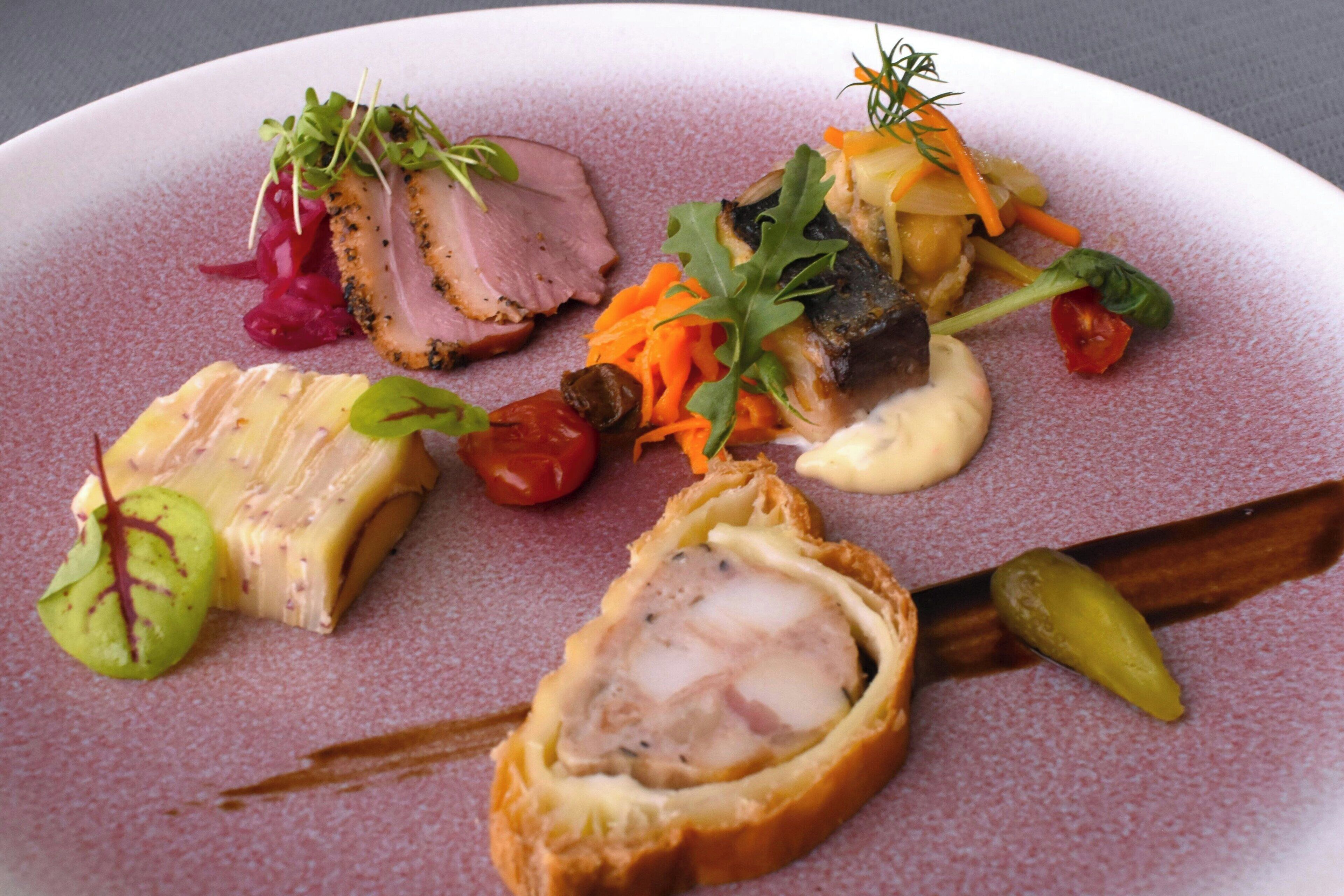 A plate of food with various dishes including a slice of meat, vegetables, and a stuffed item.