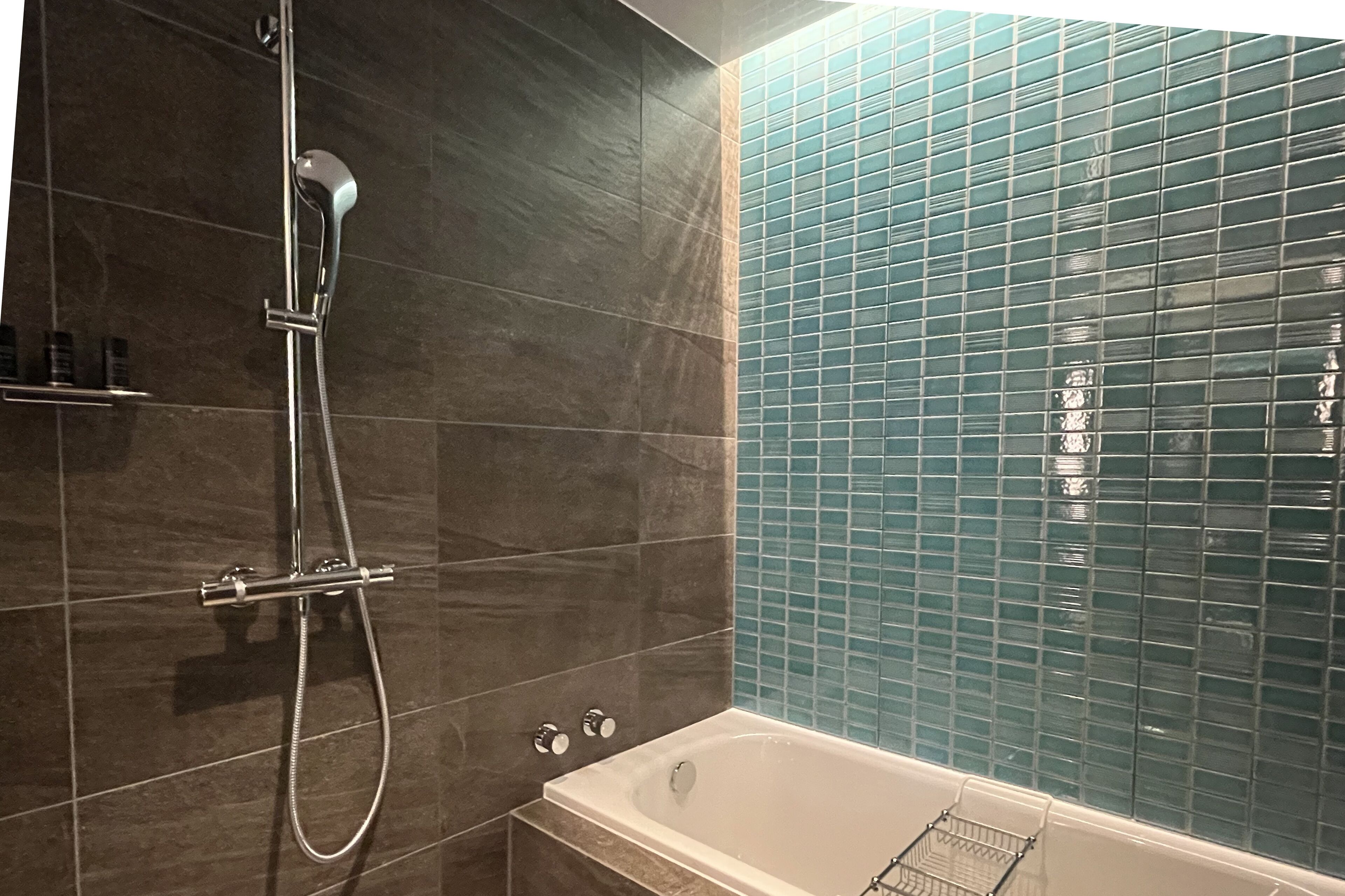 Un baño con bañera, ducha y pared de azulejos.