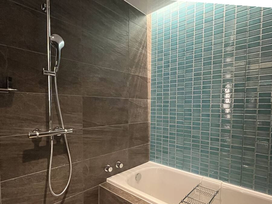 A bathroom with a bathtub, a shower, and a tiled wall.