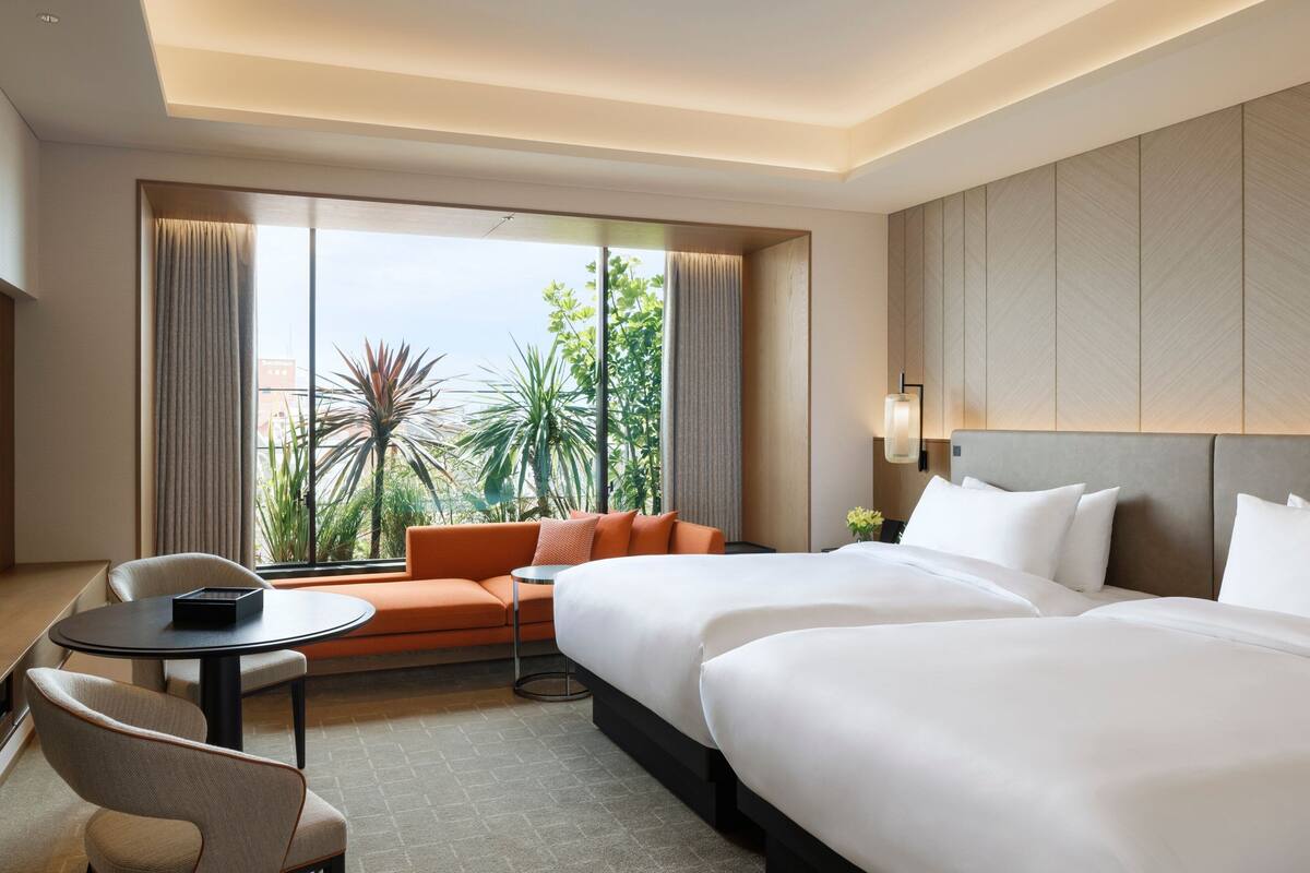 A hotel room with two beds, a sofa, a small table, and a chair.