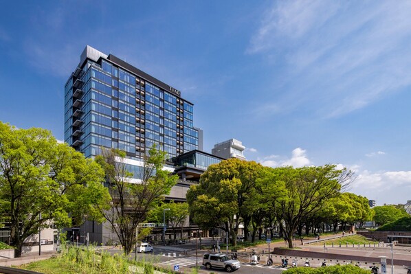 Un hotel moderno con fachada de vidrio, rodeado de vegetación exuberante y una zona peatonal.