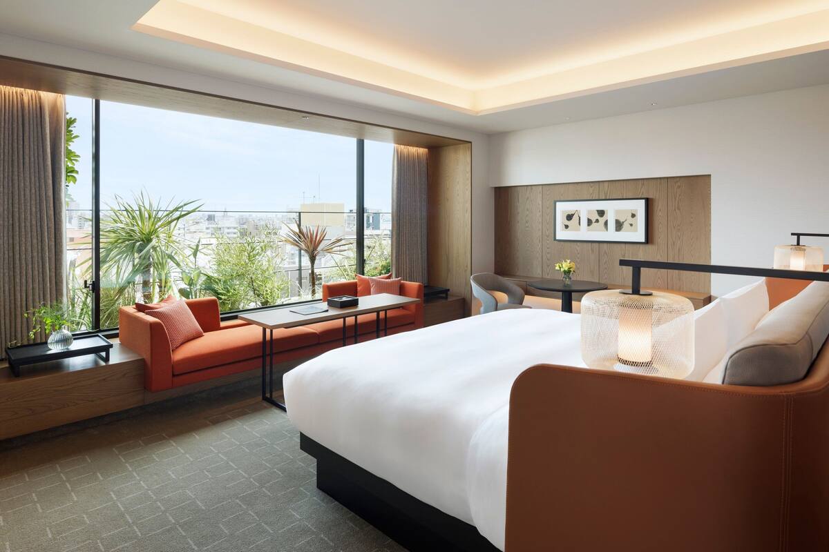 A modern hotel room with a large bed, a sofa, a dining table, and a view of the cityscape.