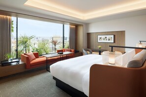 Habitación de hotel moderna con una cama grande, un sofá, una mesa de comedor y vistas a la ciudad.