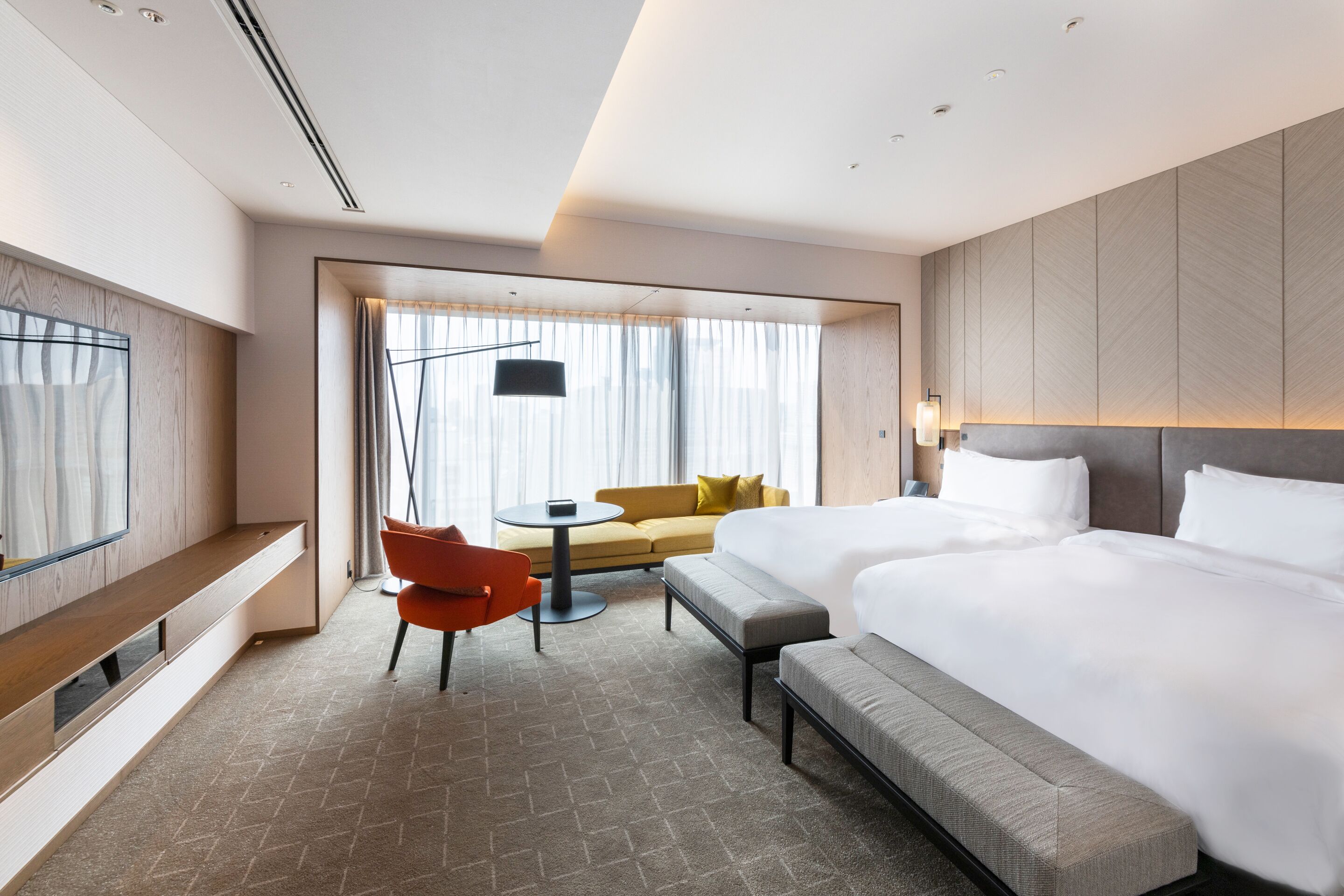 A hotel room with a large bed, a sofa, a small table, and a bench.
