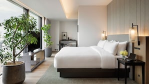 Ein modernes Hotelzimmer mit einem großen Bett, einem Schreibtisch, einem Sessel und einem Blumentopf, mit Blick auf die Stadt.
