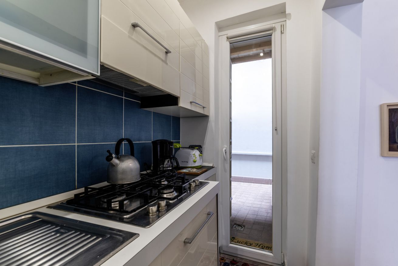 A kitchen with a gas stove, kettle, and coffee maker. There is a door leading to a balcony.