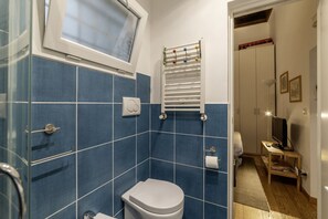 Een badkamer met blauwe tegels, een wit toilet, een handdoekhouder en een raam.
