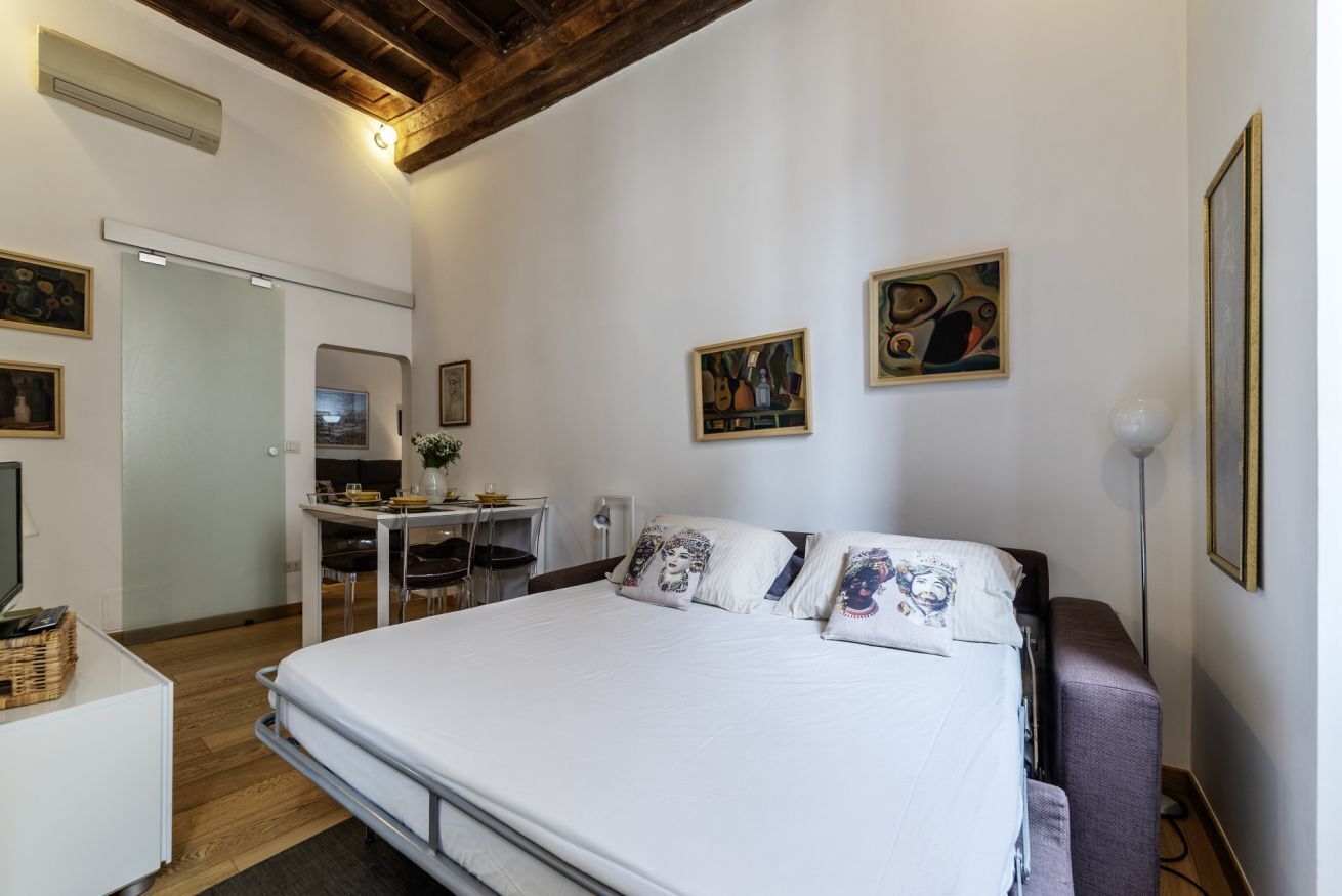A bedroom with a bed, a desk, and chairs. There are paintings on the wall.